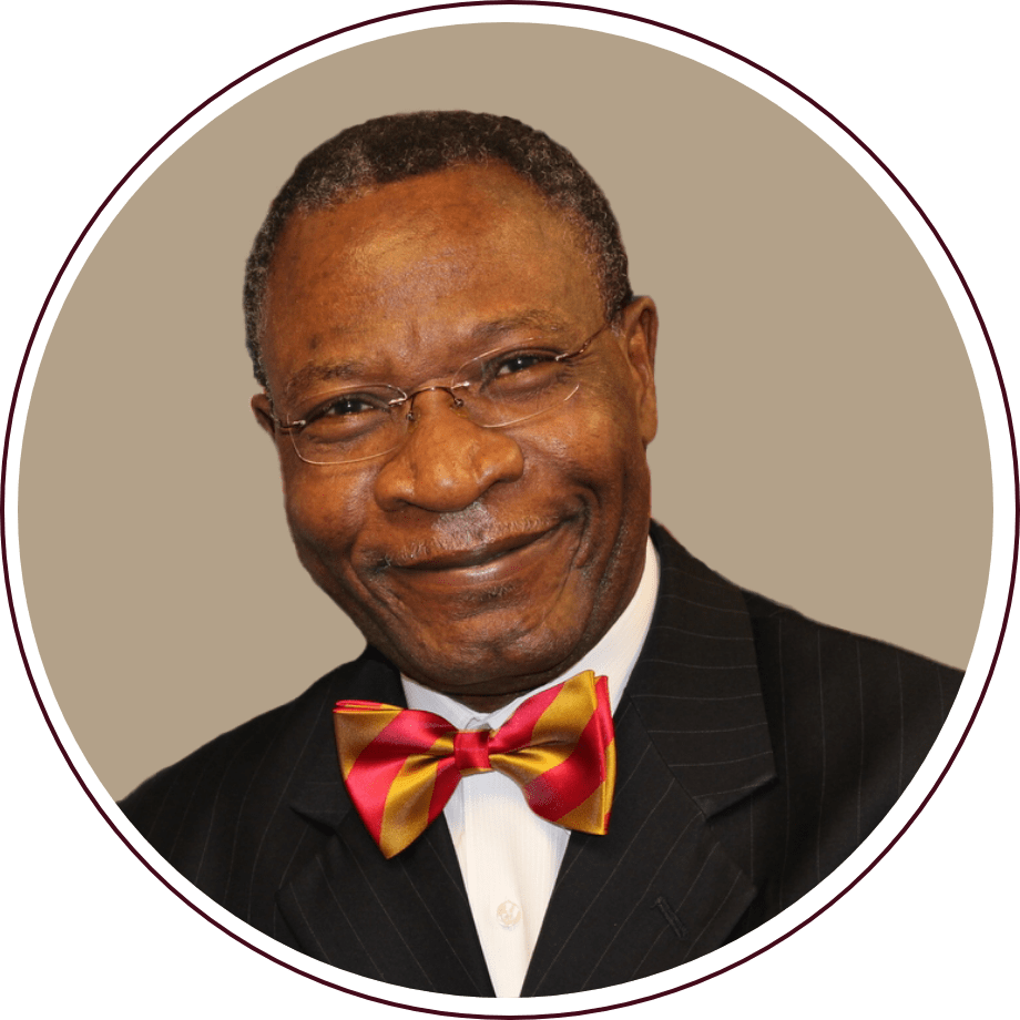 Smiling man wearing glasses and a red and gold bow tie, dressed in a pinstripe suit, against a neutral background.